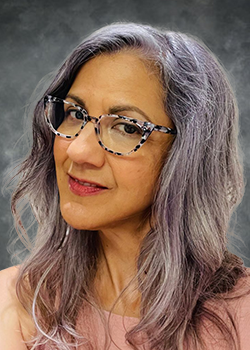 Woman with medium length grey hair wearing black and white rimmed glasses