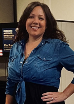 Woman with dark brown hair wearing a jean shirt tied over a black dress